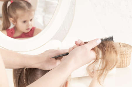 hands of mother combing a little smiling girl in a red dress