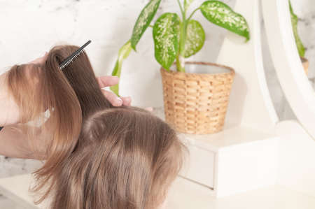 mother combing her comb little three-year-old girl in a red dressの写真素材