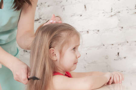 mother combing her comb little three-year-old girl in a red dressの写真素材