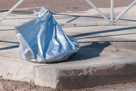A garbage bag in a blue plastic bag lies on the side of the road in summer dayの写真素材
