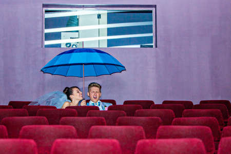 Young couple sitting under a umbrella in movie theatre on their wedding dayの写真素材