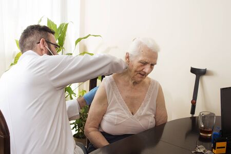 Doctor examining an old woman with a stethoscope in a doctor's office. Medical examination with a stethoscope. Geriatrician doctor examining lungs.の写真素材