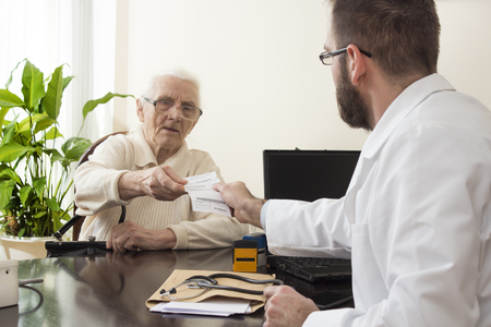 The doctor gives the patient a prescription. geriatrician doctor with a patient in his office. Old woman at the doctor geriatrician.の写真素材