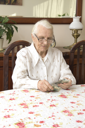The old woman counting money while sitting at the table. Pension. Old woman counts the money. Old woman with a sad face counts money while sitting at the table.の写真素材
