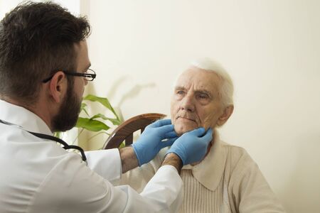 The doctor examines the lymph nodes on the neck of an old woman.の写真素材