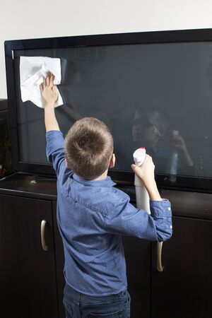 Boy with glasses during cleaning. He wipes the TV screen with dust from the cloth.の写真素材