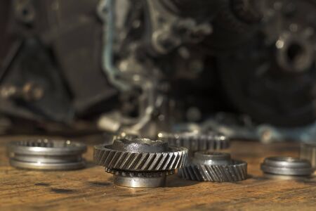 Gear wheels, damaged modes lie on a wooden table top. In the background a manual transmission from the car.の写真素材