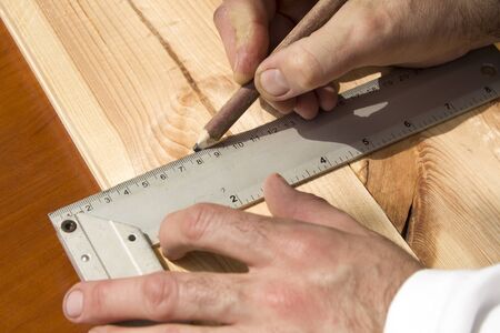 The carpenter's hands indicate the dimension on the board with a pencil and an angle.の写真素材