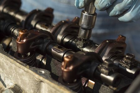 The mechanic's hand unscrews the screw in the engine with a socket wrench. Unscrewing valve tappets...