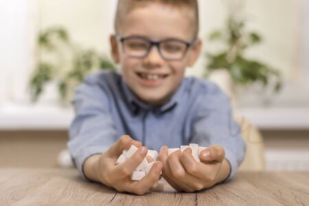 The boy's hands are full of sugar cubes in the foreground. Smiling boy face with glasses in a blue...
