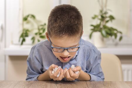 school-age boy sitting at the table. He holds a full handful of sugar cubes. His cheeks are filled...