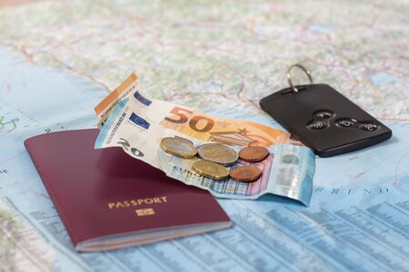 A paper road map with a passport, euro banknotes and coins and a car card.