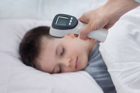 In the foreground a hand holds an electronic thermometer ready for measurement. In the background...