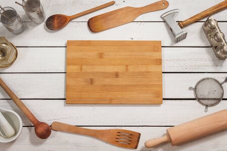 The wooden kitchen board lies on a white table. Around there are old stylish wooden kitchen utensils forming a background.の写真素材