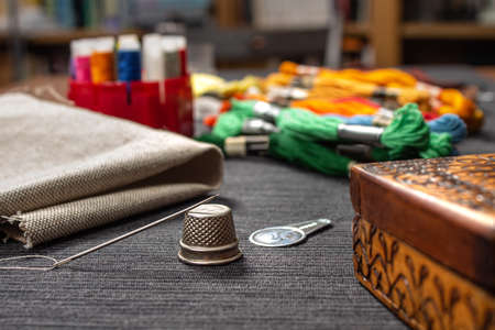 In the foreground a needle lying on a thimble. In the background, fabric and multicolored mouline...