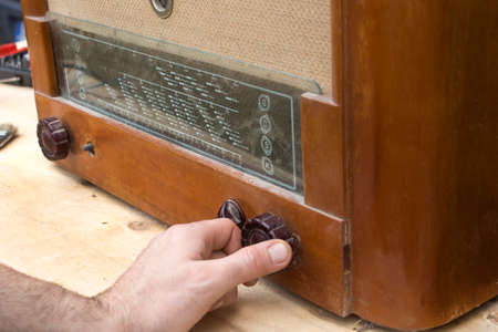 The man's hand turns on an old vintage radio lamp. The man's hand adjusts the potentiometer scale in the old vintage radio tube.の写真素材