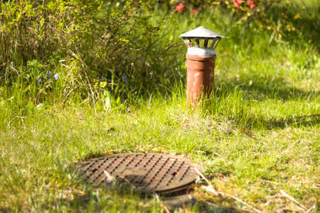 A steel cover from the cesspits and an air vent on the background of a green garden