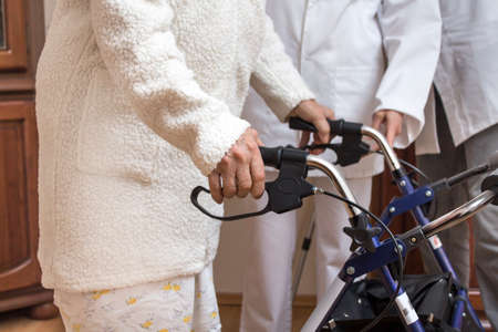 The hands of an old woman on the handles of a walker with brakes. The nurse helps the old woman.の写真素材