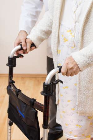 The male nurse keeps his hand on the old woman's hand, helping her to walk with the help of a small balcony.の写真素材