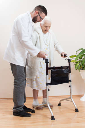 A man nurse helps a very old woman to walk with the help of a rehabilitation walker.の写真素材