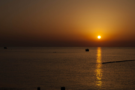 Sunrise with reflection on sea water scale of dark orange color and boatの写真素材