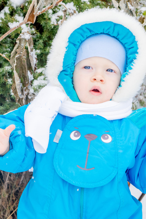 Baby boy surprised with a snow at a winter gardenの写真素材