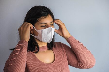 Woman in a pink sweater putting on a mask for the coronavirus