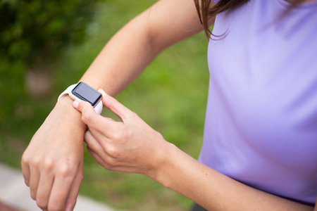 Female wearing a fitness tracker watch to monitor training in an urban park. Wellness, health and active lifestyle.の写真素材