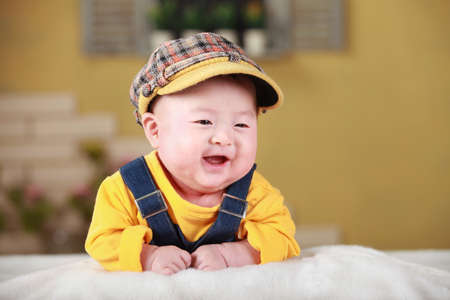 Happy cute 3-month old Chinese baby boy playing on bed with colorful suites