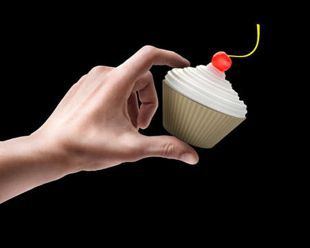 Man's hand holding cup-cake with creme fraiche and cherry isolated on black background の写真素材