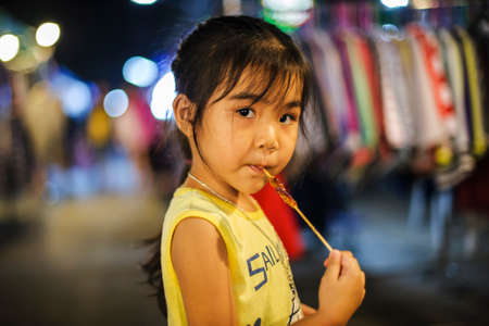 CHIANG-MAI, THAILAND - NOVEMBER 4, 2017 : The girl in a yellow shirt is eating a barbecue at the night market.のeditorial素材
