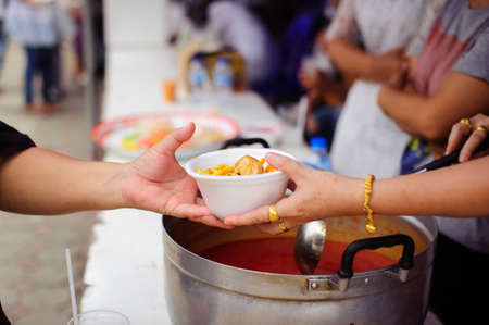 Hands of volunteers serves free food to the poor and needy in the city : The poor people bring a container to scoop food to eat and relieve hunger and bring homeの写真素材