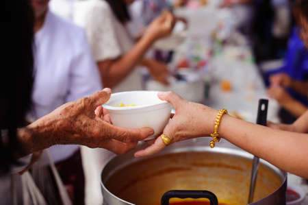 Hands of volunteers serves free food to the poor and needy in the city : The poor people bring a container to scoop food to eat and relieve hunger and bring homeの写真素材