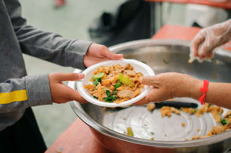Hands of volunteers serves free food to the poor and needy in the city : The poor people bring a container to scoop food to eat and relieve hunger and bring homeの写真素材