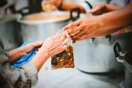 Homeless people receive free charity food from the hands of volunteers : concept of hunger problems in a helping societyの写真素材