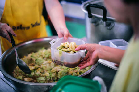 The hands of the needy holding a container to receive free charity food from volunteers : the concept of food assistanceの写真素材