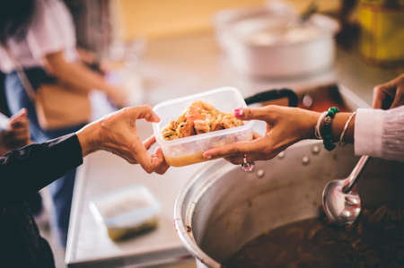 The concept of food needs in society : The recipient's hand holds a dish to request free charity food from a volunteer.の写真素材