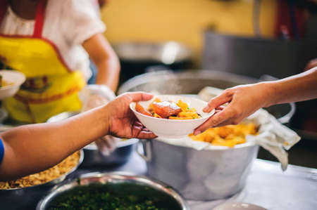 The concept of giving: Homeless people reach out to free volunteer meals from volunteers: help feed the hungry in society.の写真素材