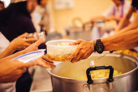 The concept of giving: Homeless people reach out to free volunteer meals from volunteers: help feed the hungry in society.の写真素材