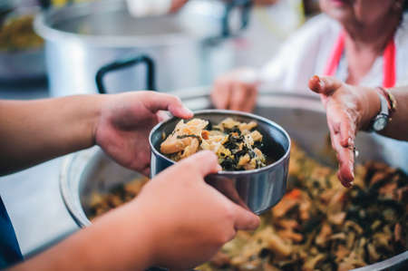 The hands of the poor handed a plate to receive food from volunteers to alleviate hunger, the concept of helping the homeless.の写真素材