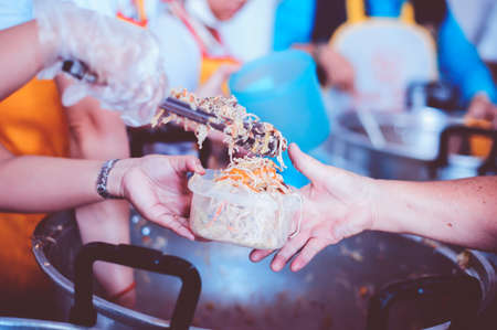 The hand of the wanderer extends to receive food from donations. With volunteers scooping food: the idea of helping with hungerの写真素材