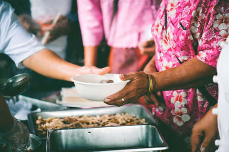 Poor people carrying plates receive food donations from volunteers : The concept of helpingの写真素材