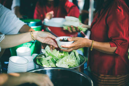Poor people carrying plates receive food donations from volunteers : The concept of helpingの写真素材