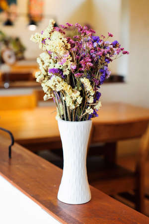 A bouquet of dried flowers in a tall white flower vase