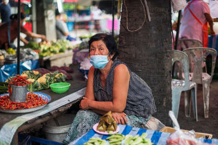 CHIANG MAI, THAILAND - JULY 30, 2021:  A woman wearing masks sits selling edamame on a stall at an open-air market in Chiang Mai, Thailand.のeditorial素材