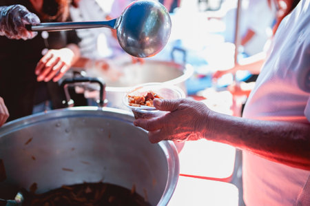 The hand of the wanderer extends to receive food from donations. With volunteers scooping food: the idea of helping with hungerの写真素材