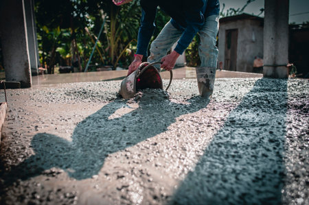 Manually pouring concrete for a surface adjustment on a construction site.