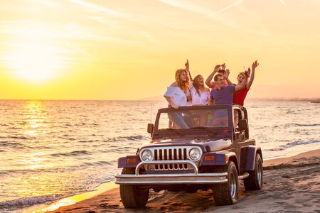 Young group having fun on the beach drink beer and dancing in a convertible carの写真素材