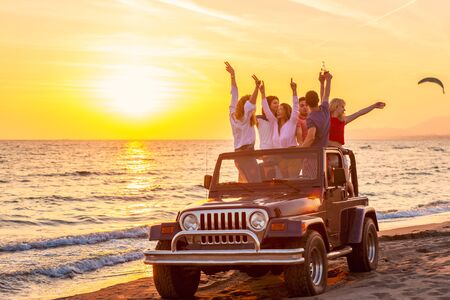 Young group having fun on the beach drink beer and dancing in a convertible carの写真素材