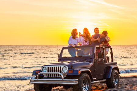 Young group having fun on the beach drink beer and dancing in a convertible carの写真素材
